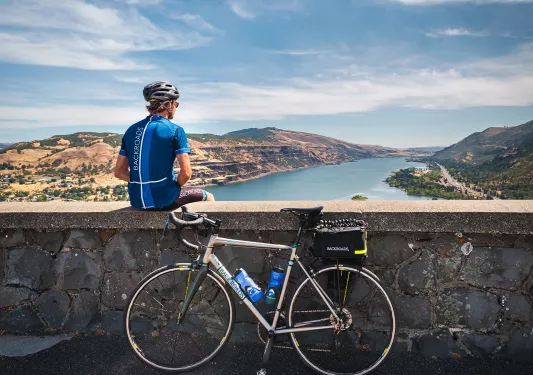 Man sitting on a stone ledge looking out to a lake, with a bike leaning on the ledge