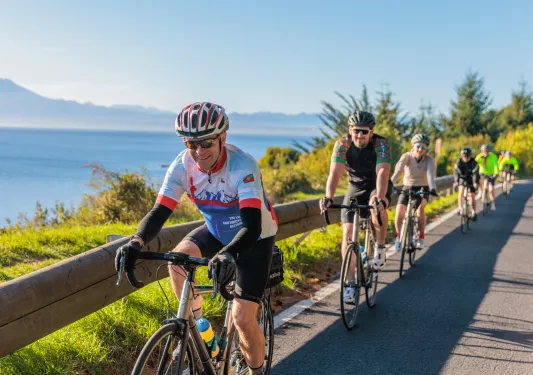 Group of people biking in a single line on a road with the ocean to the left