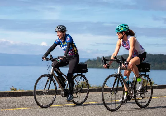 Man and woman riding their bikes on an empty road with a large lake in the background