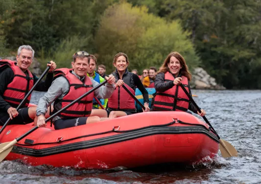 Group of people wearing life vests while paddling in a red raft on a river