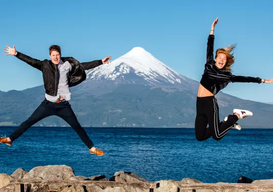 Man and woman jumping, with a large lake and mountain in the background