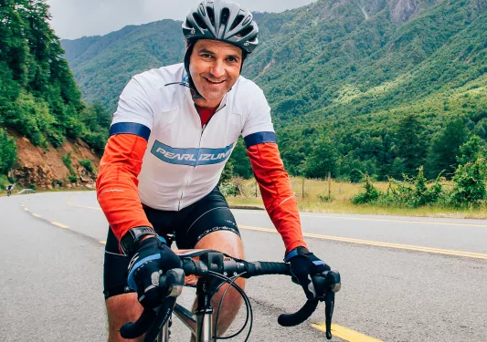 Man wearing biking gear and riding a bike on a road, with mountains in the background