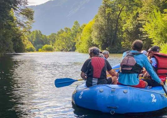 Group of people on a blue raft, paddling in the middle of a river