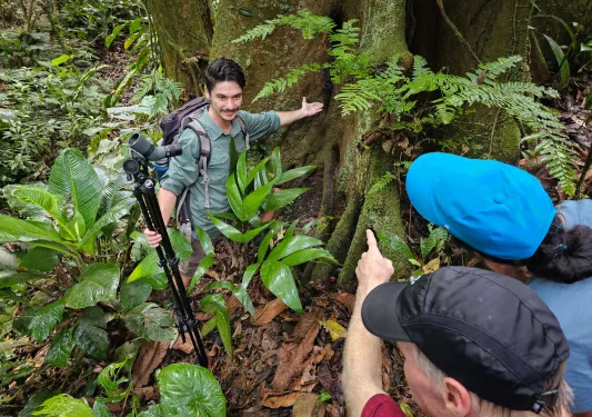 Man holding tripod wile pointing to a large tree