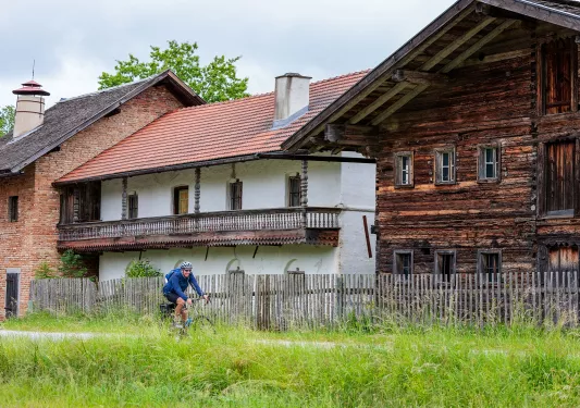 Man riding a bike on an empty road with wooden houses in the background