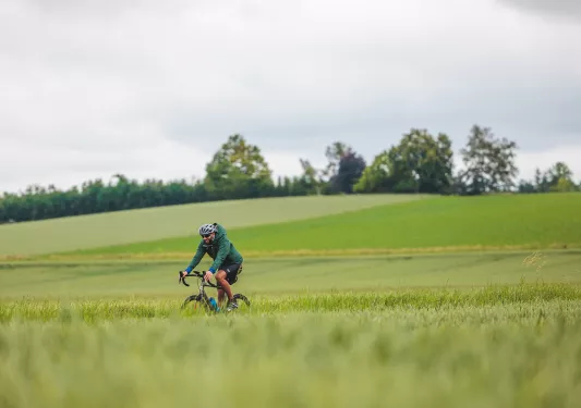 Man riding a bike on a road next to an empty valley of grass