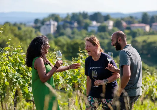 Two women and one man standing in a vineyard while holding glasses of wine