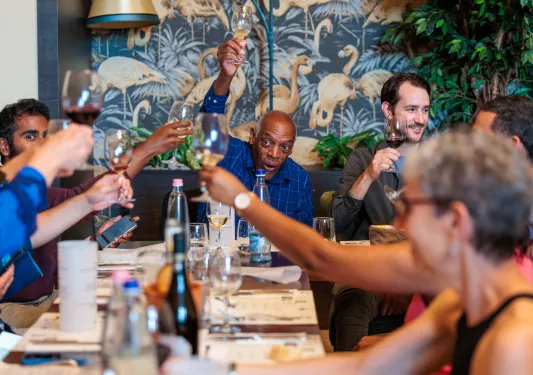 Group of people laughing and raising glasses of wine around a dining table