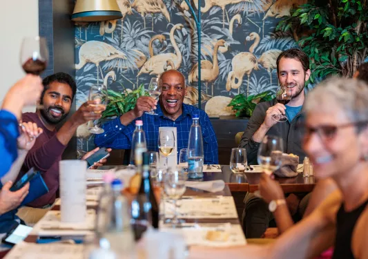 Group of people smiling at a dining table, raising their glasses of wine