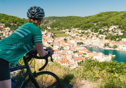 Woman leaning on a bike, looking out towards a small town