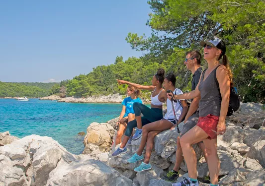 Group of people sitting on rocks next to the ocean, pointing and smiling