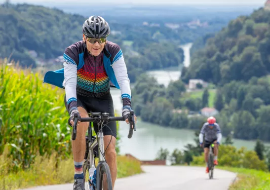 Man smiling while biking on a road, with a river in the distance