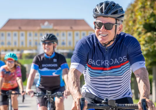 Man and two women smiling while biking, with a large yellow building in the background