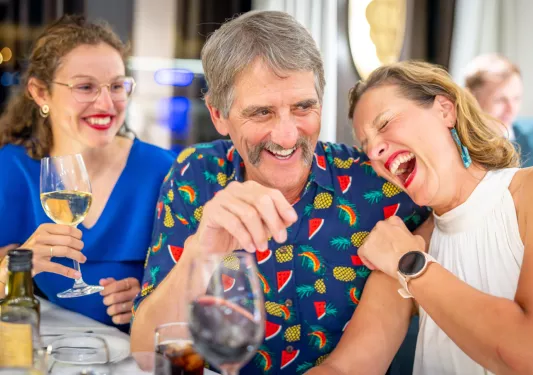 One man and two women, smiling and laughing while holding wine glasses