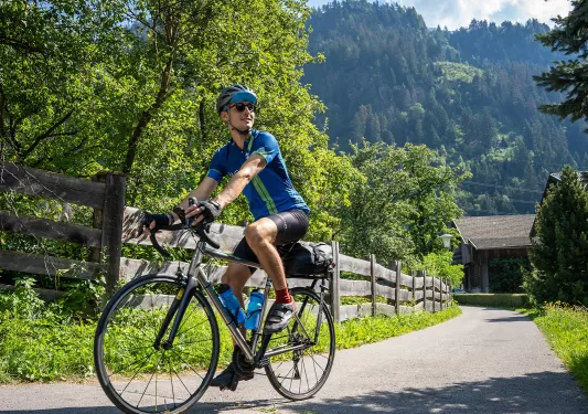 Person riding a bike on an empty road with a large forest in the background