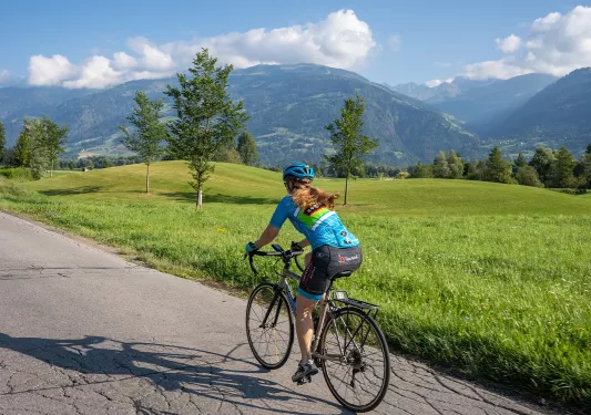 Woman riding a bike on an empty road, with a large valley to the right