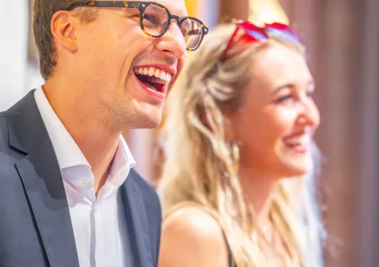 Man wearing a suit and a woman in the back smiling