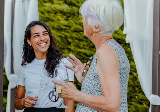 Two women smiling and talking, while holding glasses of wine