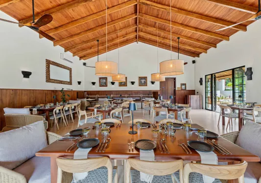 Restaurant dining hall with wooden tables and cushioned chairs, and circular light fixtures