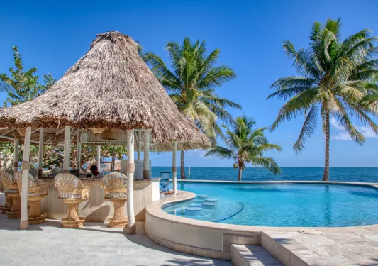 Outdoor pool with a straw hut to the left and the beach in the background