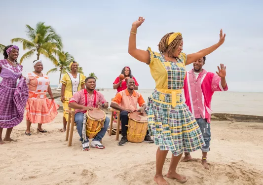Two men playing large drums with a group of women dancing