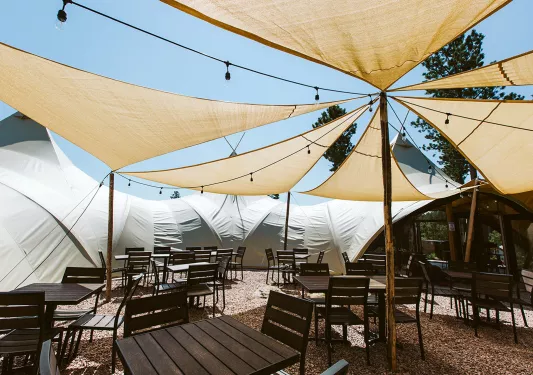 Outdoor patio on gravel, with large cloth sun shades and wooden chairs