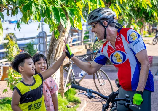 Man riding a bike while giving high fives to little kids