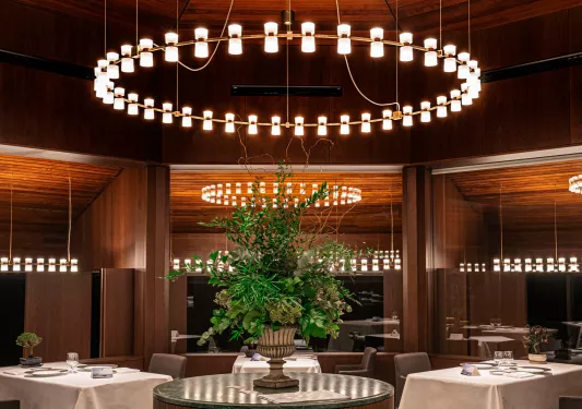 Restaurant with a circular light fixture and white dining tables around a floral centerpiece