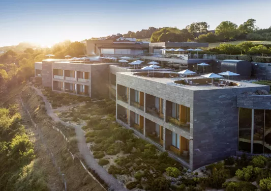 Exterior view of stone hotel building with a rooftop patio and trees in the distance