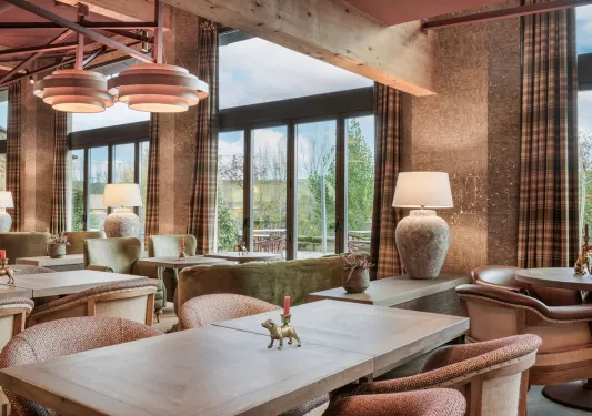 Lounge and seating area with wooden table and cushioned chairs, with large windows in the back