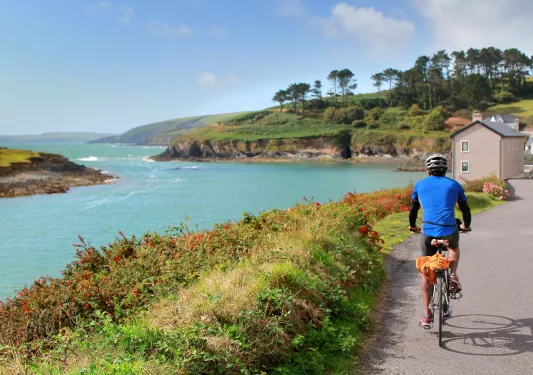 Man in a blue jersey, riding a bike on a road along a large lake