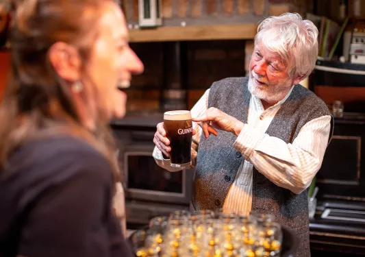 Man pointing to a pint of Guinness beer, while a woman in front is smiling