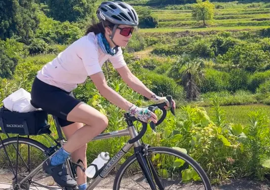 Woman riding bike on a path with large forest in the back