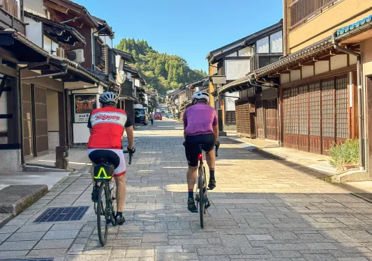 Two men biking on a stone road in the middle of a Japanese town
