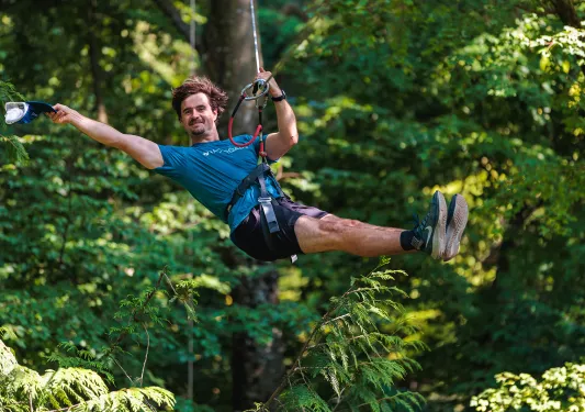 Man on a zipline, smiling while holding his hat