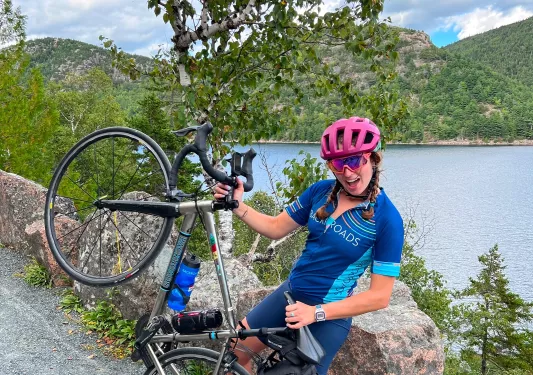 Woman leading on a rock, smiling with holding up her bicycle