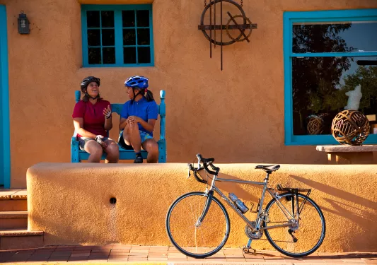 Two women sitting in front of an orange house, with a bike parked out front