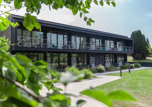 Exterior view of black, two-story building with outdoor balconies and a grass field in front