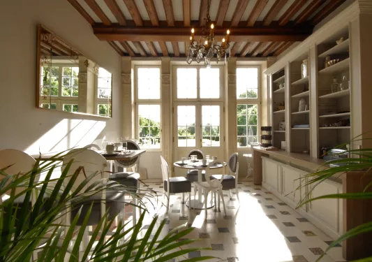 Kitchen with two dining tables and white and blue chairs, with large windows in the background