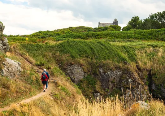 Man and woman walking on a dirt trail with grassy hills to the right