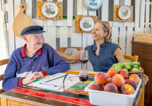 Older man sitting with a woman, smiling with two wine glasses on a table in front