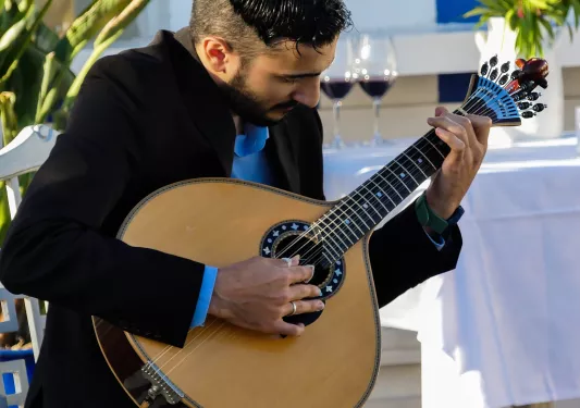 Man playing a guitar with a white table with wine glasses in the background