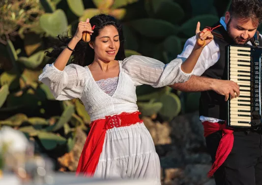 Woman in a white dress, dancing with a man playing the accordion to her left