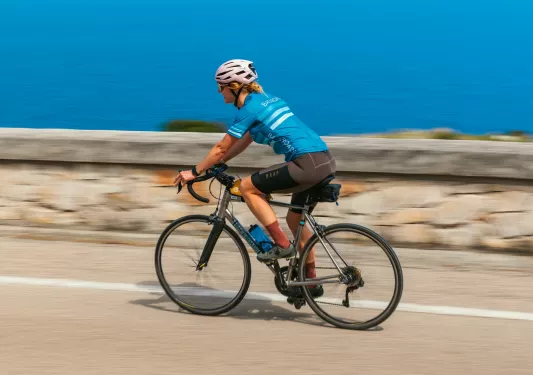 Woman riding a bike on a road with the ocean in the background
