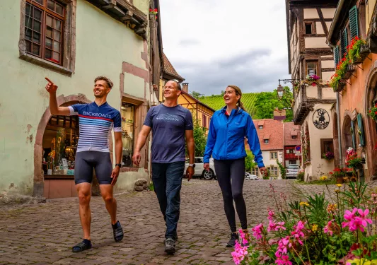 Two men and one woman walking on a stone alleyway, pointing and smiling