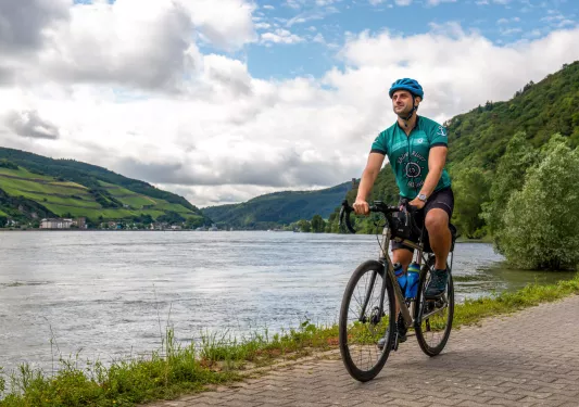 Man riding a bike on a stone path, next to a large lake