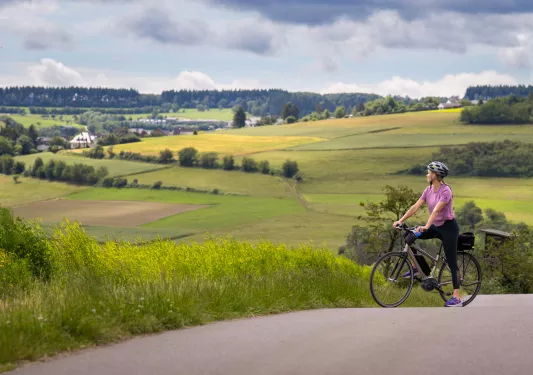 Woman riding a bike on top of a hill, looking out towards a valley of crops