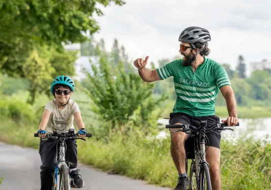 Man and son riding their bikes on a road, with a lake on the right