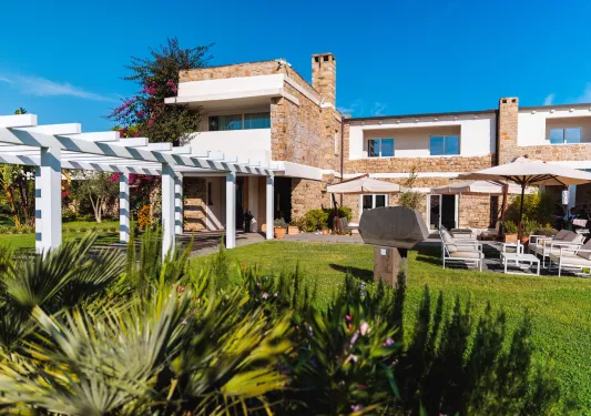 Exterior view of stone and white building with a garden and grass area in front