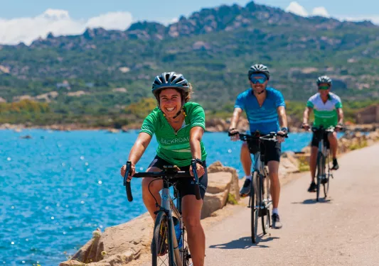 One woman and two men riding bikes on an empty road next to a large lake
